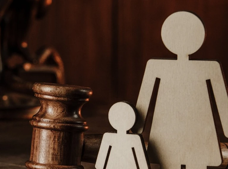 Wooden chess rook and two beige wooden human figures, one large and one small, on a dark brown background.