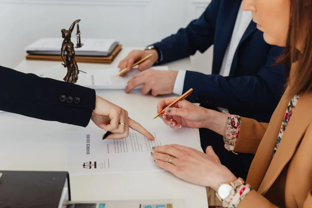 Two professionals reviewing and signing a divorce decree document at a white desk.