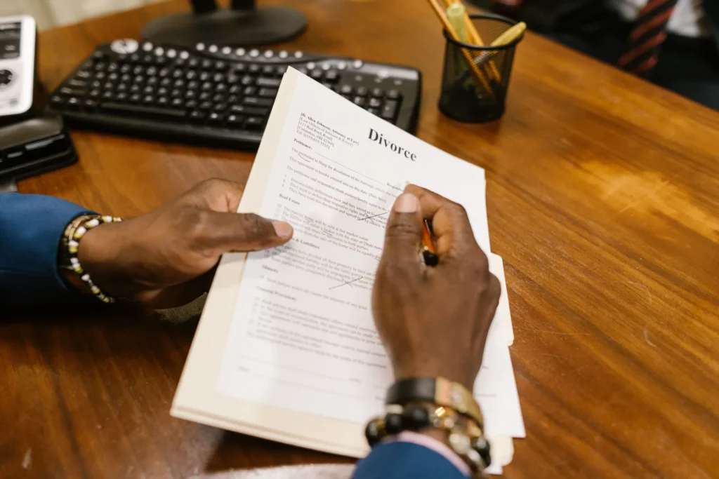 Person signing a divorce document on a wooden desk with office supplies nearby.
