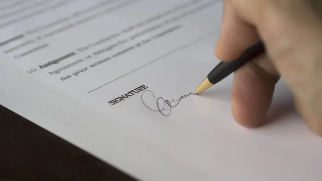 Close-up of a hand signing a document with a black and gold pen on a white paper.