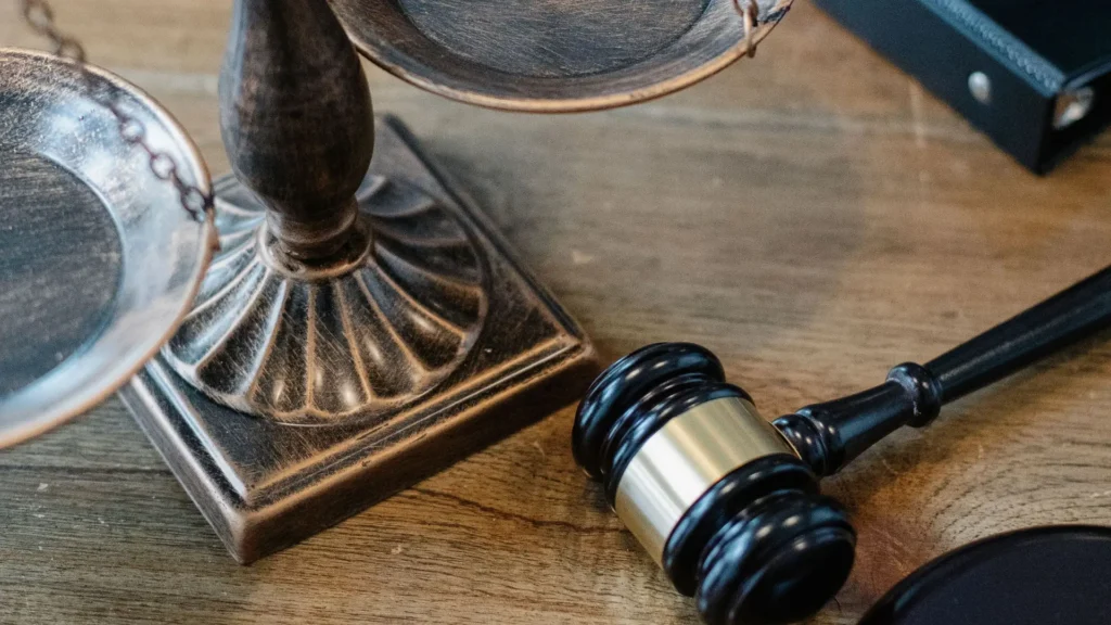 Close-up of a wooden judge's gavel and bronze balance scales on a wooden surface.