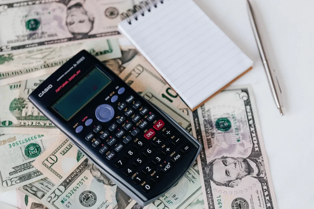 Scientific calculator, blank notepad, and pen on scattered US dollar bills.