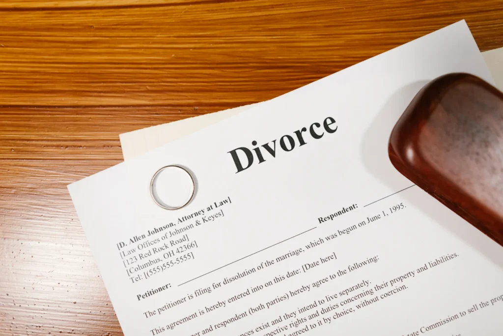 Legal divorce document on wooden table with wedding ring and judge's gavel.