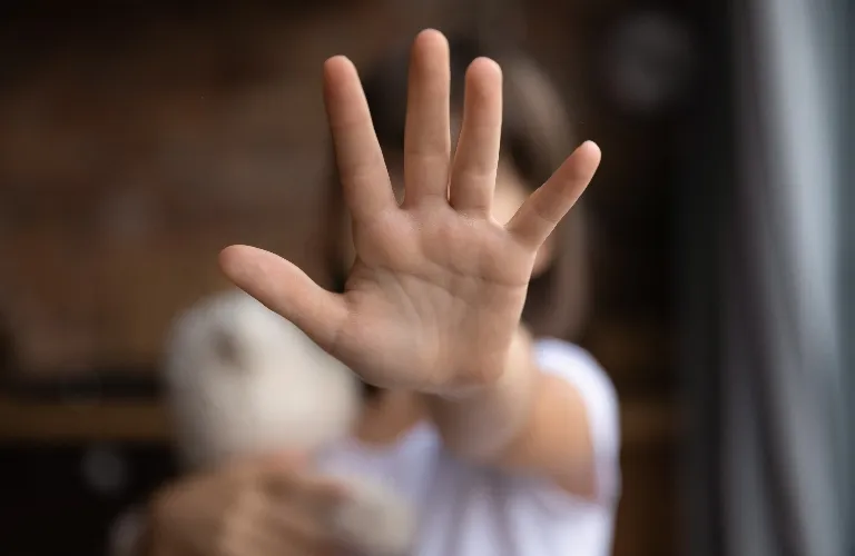 Close-up of an outstretched hand obscuring a person holding a teddy bear indoors.